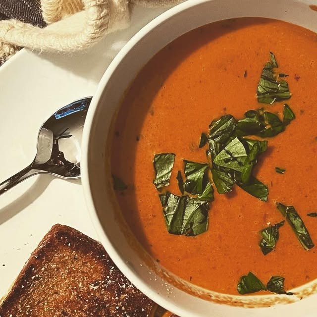A bowl of tomato soup with fresh basil and toast